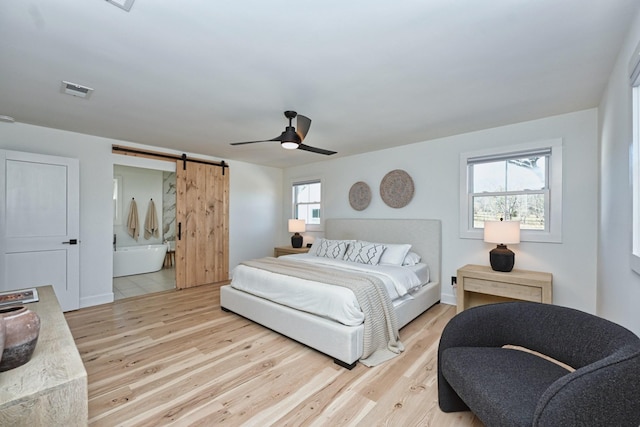 bedroom featuring ceiling fan, a barn door, multiple windows, and light hardwood / wood-style flooring