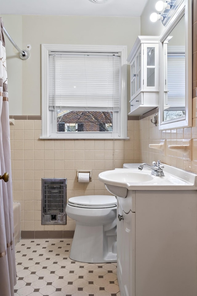 full bathroom featuring heating unit, tile walls, vanity, toilet, and shower / bath combo with shower curtain