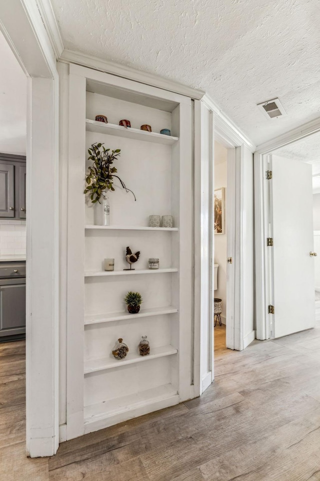 hallway featuring a textured ceiling, crown molding, and light wood-type flooring