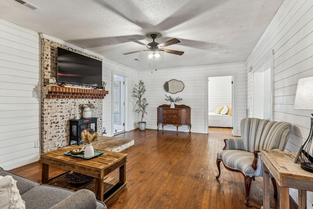 living room with ceiling fan, wooden walls, a wood stove, a textured ceiling, and dark hardwood / wood-style flooring