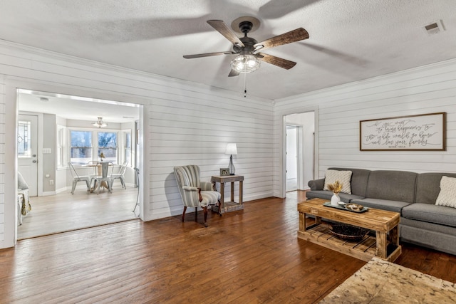 living room with ceiling fan with notable chandelier, a textured ceiling, dark hardwood / wood-style floors, and wood walls