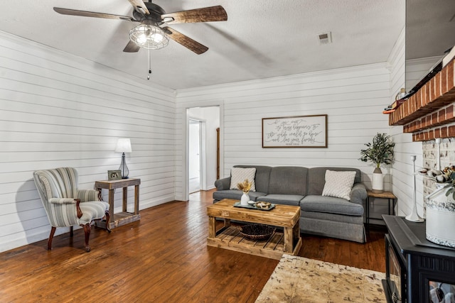 living room featuring a textured ceiling, ceiling fan, dark hardwood / wood-style floors, and wooden walls