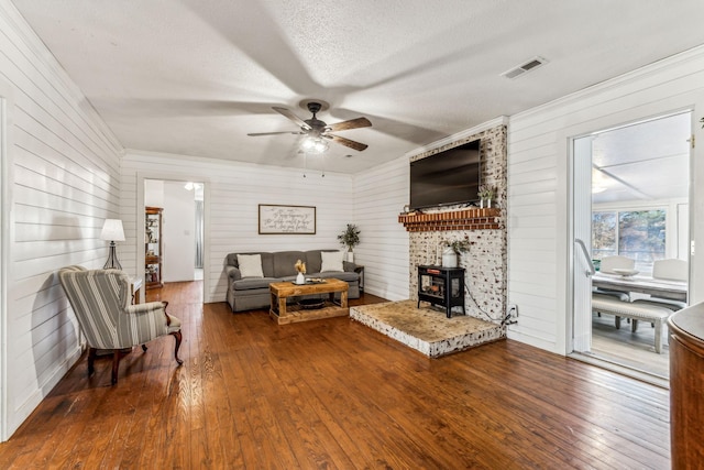 living room featuring ceiling fan, a textured ceiling, a wood stove, and hardwood / wood-style floors