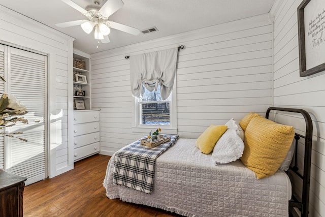 bedroom with dark wood-type flooring, ceiling fan, a closet, and wood walls