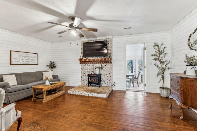 living room featuring ceiling fan, wood walls, a wood stove, a textured ceiling, and dark hardwood / wood-style flooring