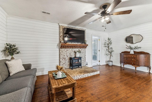 living room featuring a textured ceiling, dark hardwood / wood-style flooring, a wood stove, wood walls, and ceiling fan