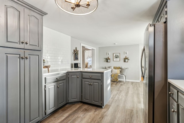 kitchen with kitchen peninsula, dark wood-type flooring, stainless steel refrigerator, and gray cabinets