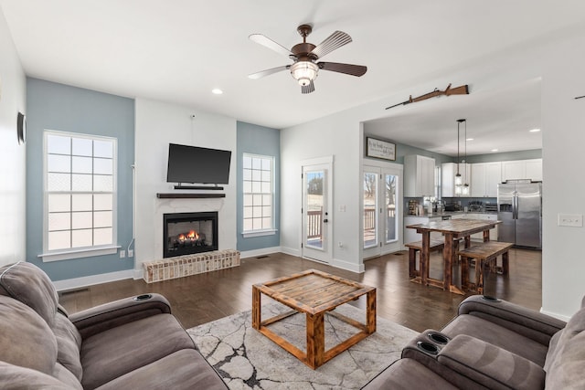 living room with dark hardwood / wood-style flooring, ceiling fan, and a healthy amount of sunlight