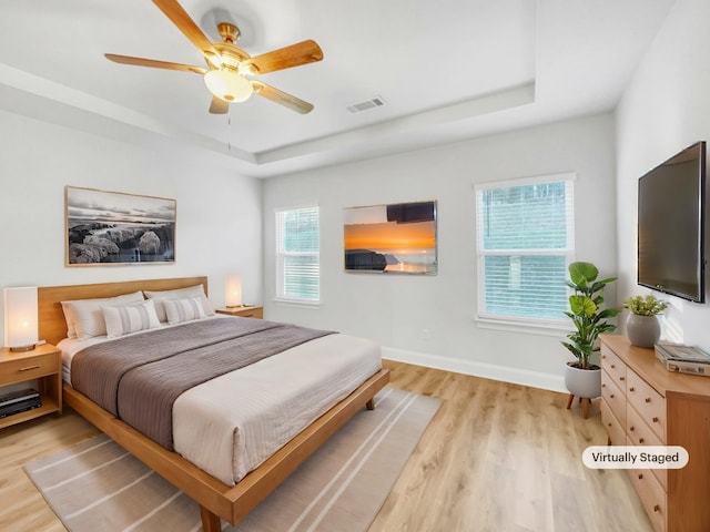 bedroom with ceiling fan, a raised ceiling, and light wood-type flooring