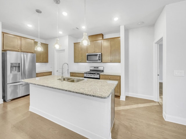 kitchen featuring pendant lighting, appliances with stainless steel finishes, an island with sink, sink, and light stone counters