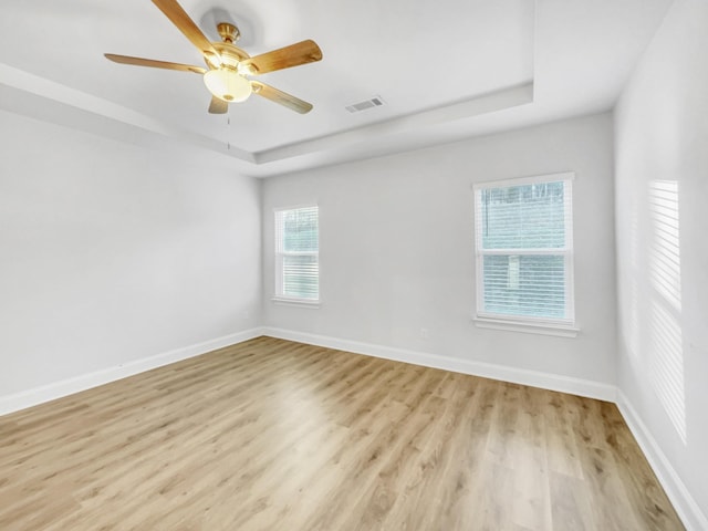 spare room featuring light wood-type flooring, ceiling fan, a healthy amount of sunlight, and a raised ceiling