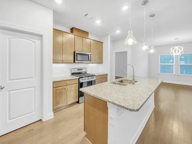 kitchen with appliances with stainless steel finishes, an island with sink, sink, hanging light fixtures, and light wood-type flooring