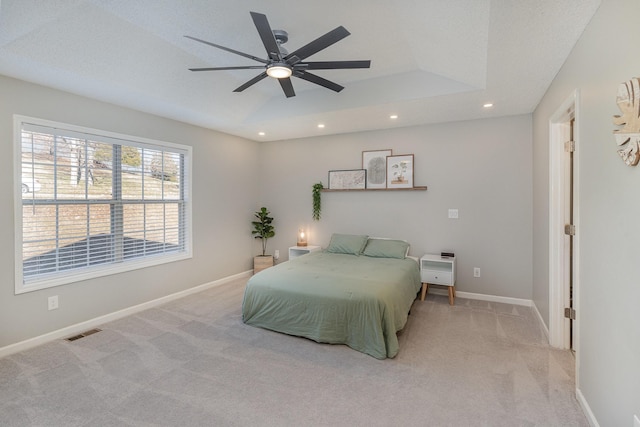 bedroom featuring ceiling fan, light colored carpet, a textured ceiling, and a raised ceiling