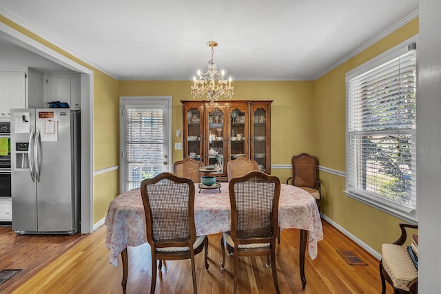 dining area with a notable chandelier, ornamental molding, and light hardwood / wood-style flooring