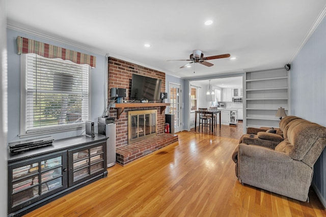 living room with a brick fireplace, ceiling fan with notable chandelier, ornamental molding, and hardwood / wood-style flooring