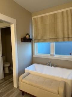 bathroom with a washtub, hardwood / wood-style floors, and toilet