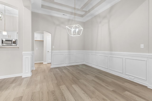 unfurnished dining area with light hardwood / wood-style floors, a raised ceiling, and ornamental molding