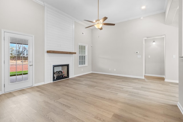 unfurnished living room with ceiling fan, a large fireplace, ornamental molding, and light hardwood / wood-style flooring