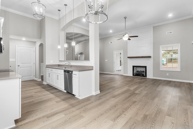 kitchen featuring stainless steel dishwasher, a large fireplace, a towering ceiling, white cabinetry, and ceiling fan with notable chandelier