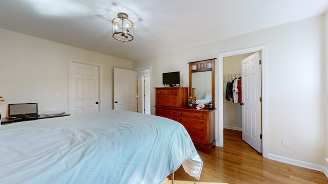 bedroom featuring a spacious closet, a chandelier, light hardwood / wood-style floors, and a closet