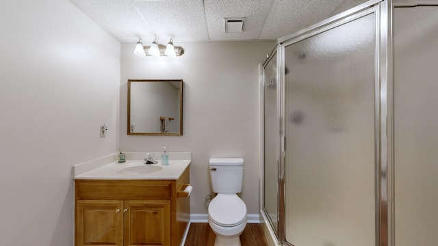 bathroom featuring toilet, vanity, a shower with door, hardwood / wood-style flooring, and a drop ceiling