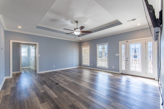 empty room featuring a raised ceiling, plenty of natural light, dark hardwood / wood-style flooring, and crown molding