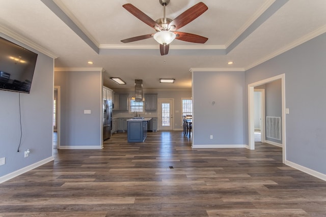 unfurnished living room with a raised ceiling, ceiling fan, dark wood-type flooring, and crown molding