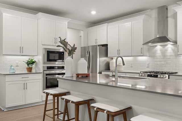 kitchen with wall chimney exhaust hood, white cabinetry, stainless steel appliances, a kitchen breakfast bar, and sink