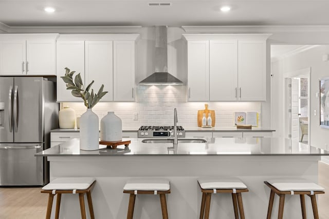 kitchen with stainless steel fridge with ice dispenser, a kitchen island with sink, wall chimney range hood, white cabinets, and a breakfast bar