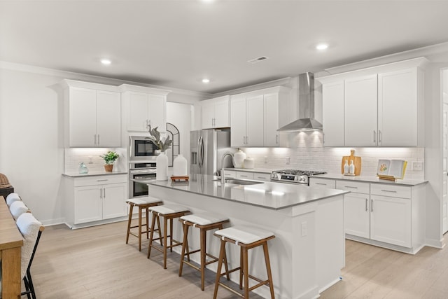 kitchen with stainless steel appliances, an island with sink, white cabinets, and wall chimney range hood