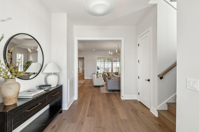 hallway with a notable chandelier, wood finished floors, visible vents, baseboards, and stairway