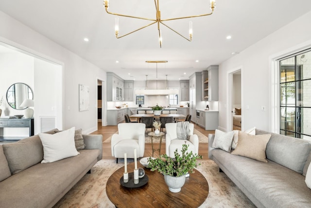 living room with a notable chandelier, recessed lighting, visible vents, light wood-style flooring, and baseboards