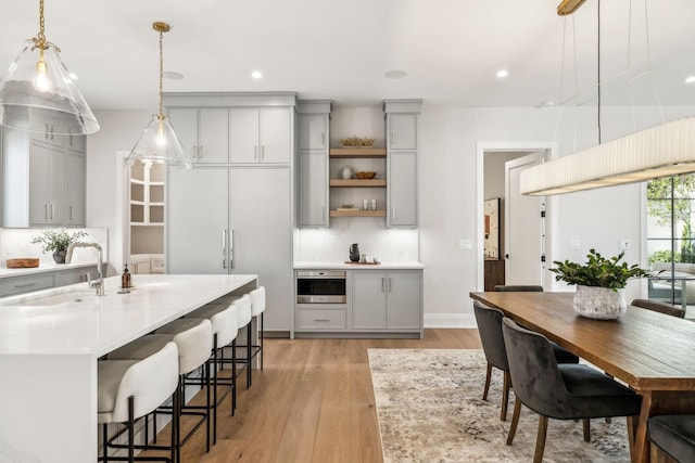 kitchen with open shelves, tasteful backsplash, gray cabinets, light countertops, and a sink