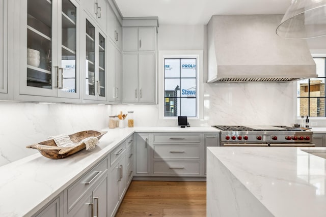 kitchen featuring gray cabinets, stainless steel stove, wall chimney range hood, and wood finished floors