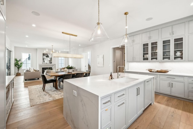 kitchen featuring a center island with sink, light wood-style flooring, glass insert cabinets, a fireplace, and a sink