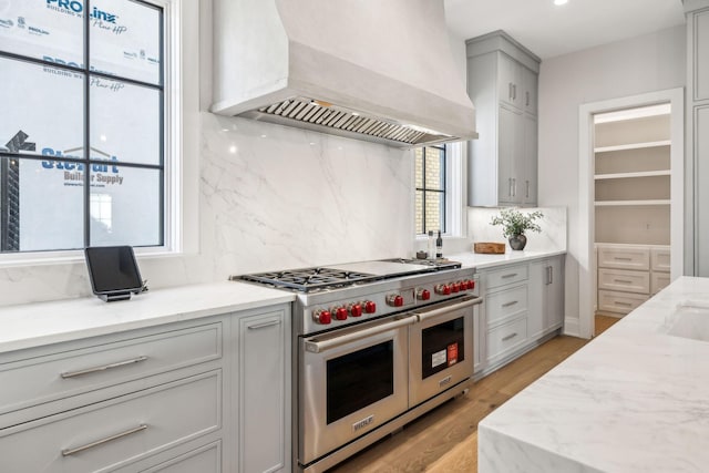 kitchen with range with two ovens, light stone counters, custom range hood, gray cabinetry, and light wood-type flooring