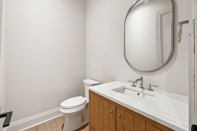 half bathroom with toilet, baseboards, wood finished floors, and vanity