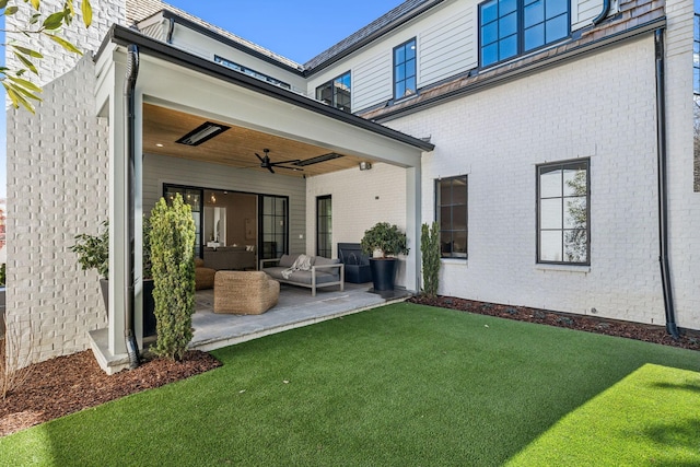 rear view of property featuring a yard, brick siding, a patio area, and a ceiling fan