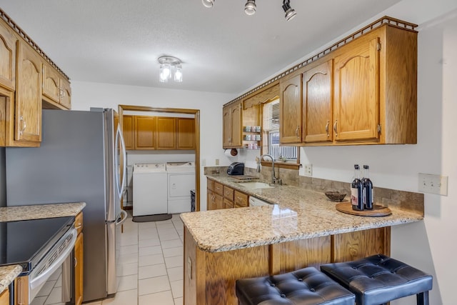 kitchen featuring separate washer and dryer, a kitchen bar, sink, kitchen peninsula, and light tile patterned floors