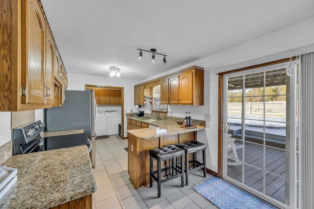 kitchen featuring light tile patterned floors, sink, washer and clothes dryer, kitchen peninsula, and a breakfast bar