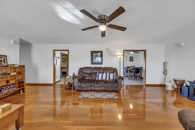 living room with light hardwood / wood-style floors, a textured ceiling, and ceiling fan