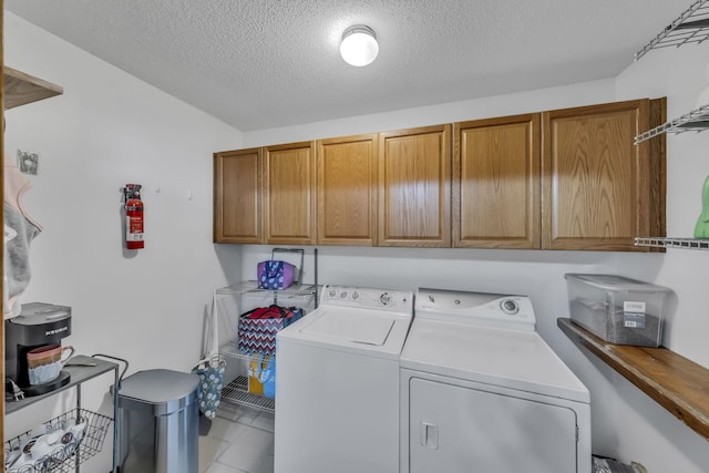 laundry area with washer and clothes dryer, a textured ceiling, cabinets, and tile patterned flooring