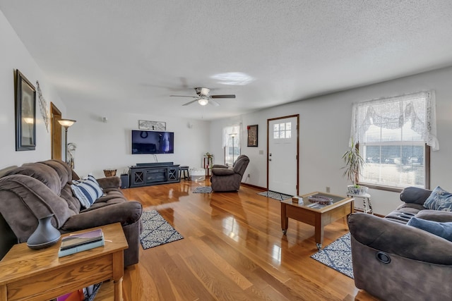 living room with light wood-type flooring, ceiling fan, and a textured ceiling