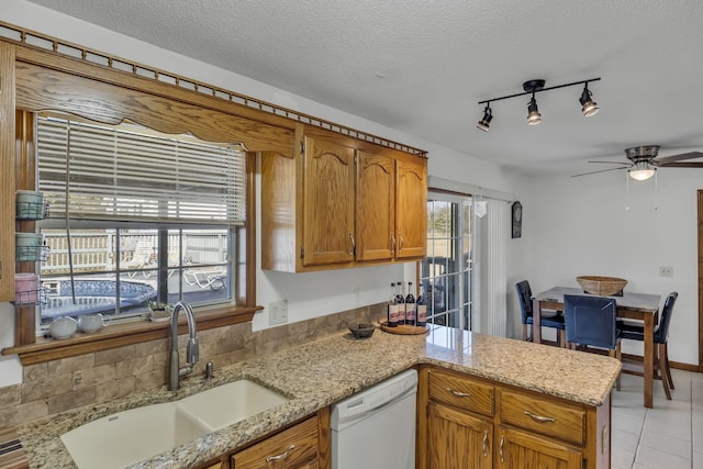 kitchen with kitchen peninsula, white dishwasher, sink, light stone counters, and a textured ceiling