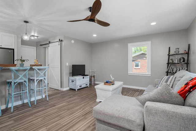 living room featuring ceiling fan, a barn door, and wood-type flooring