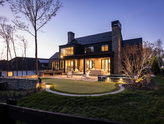 back house at dusk featuring a patio area and an in ground hot tub