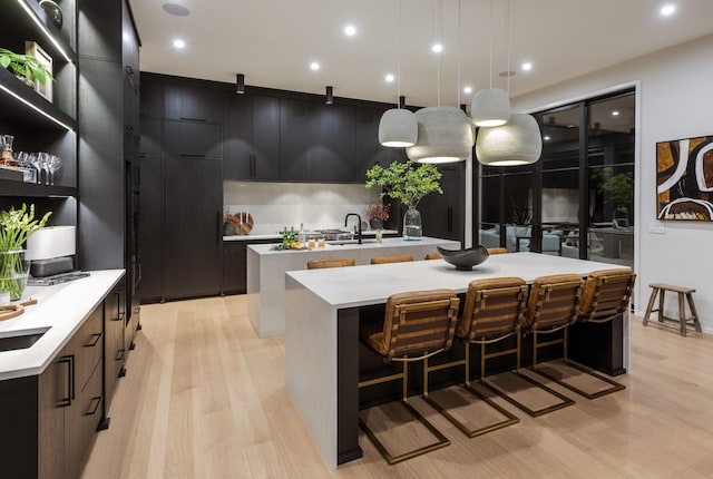 kitchen with light wood-type flooring, a large island with sink, hanging light fixtures, and a kitchen bar