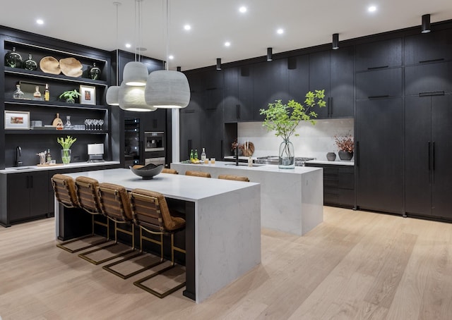 kitchen featuring decorative light fixtures, light hardwood / wood-style floors, a kitchen bar, sink, and a large island