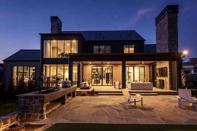 back house at dusk featuring a patio and exterior fireplace