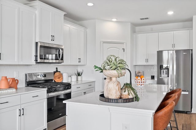 kitchen featuring light stone countertops, white cabinetry, stainless steel appliances, a kitchen breakfast bar, and a kitchen island with sink